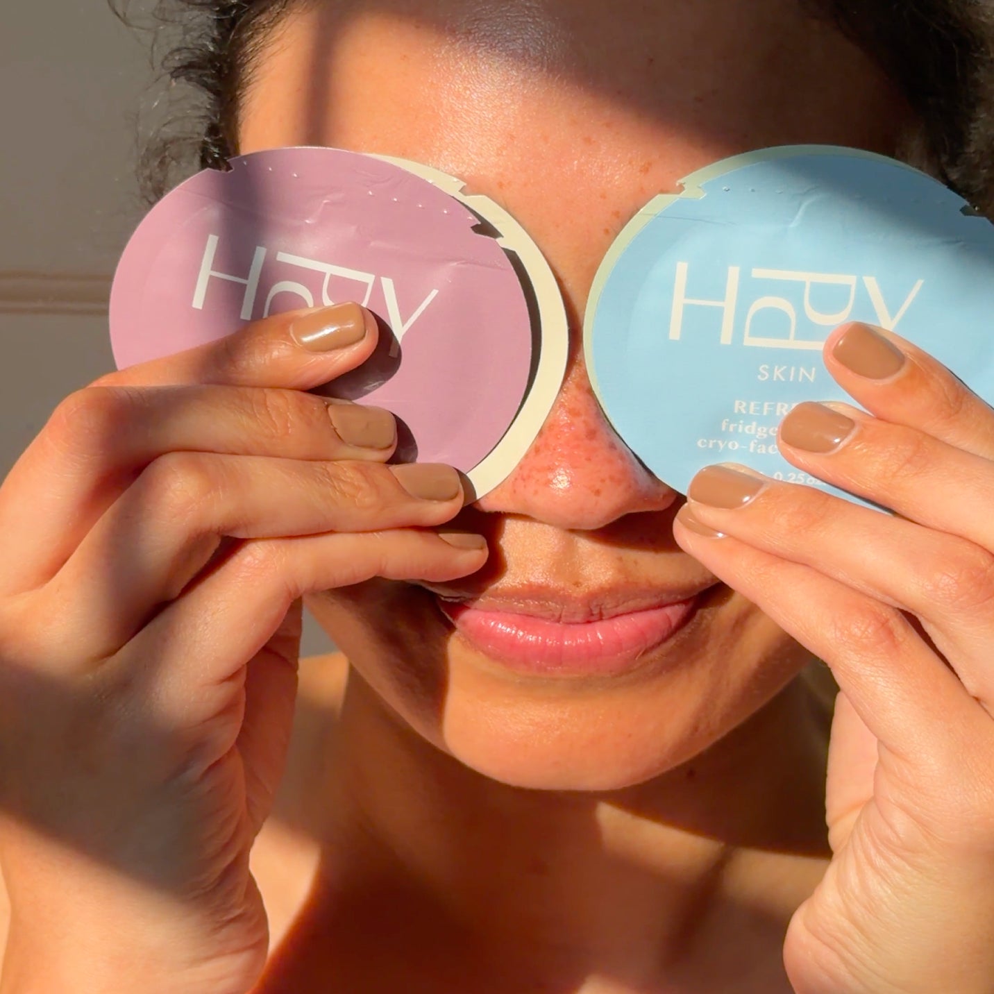 Person holding two compact mirrors with 'HPPY' branding in front of their face.
