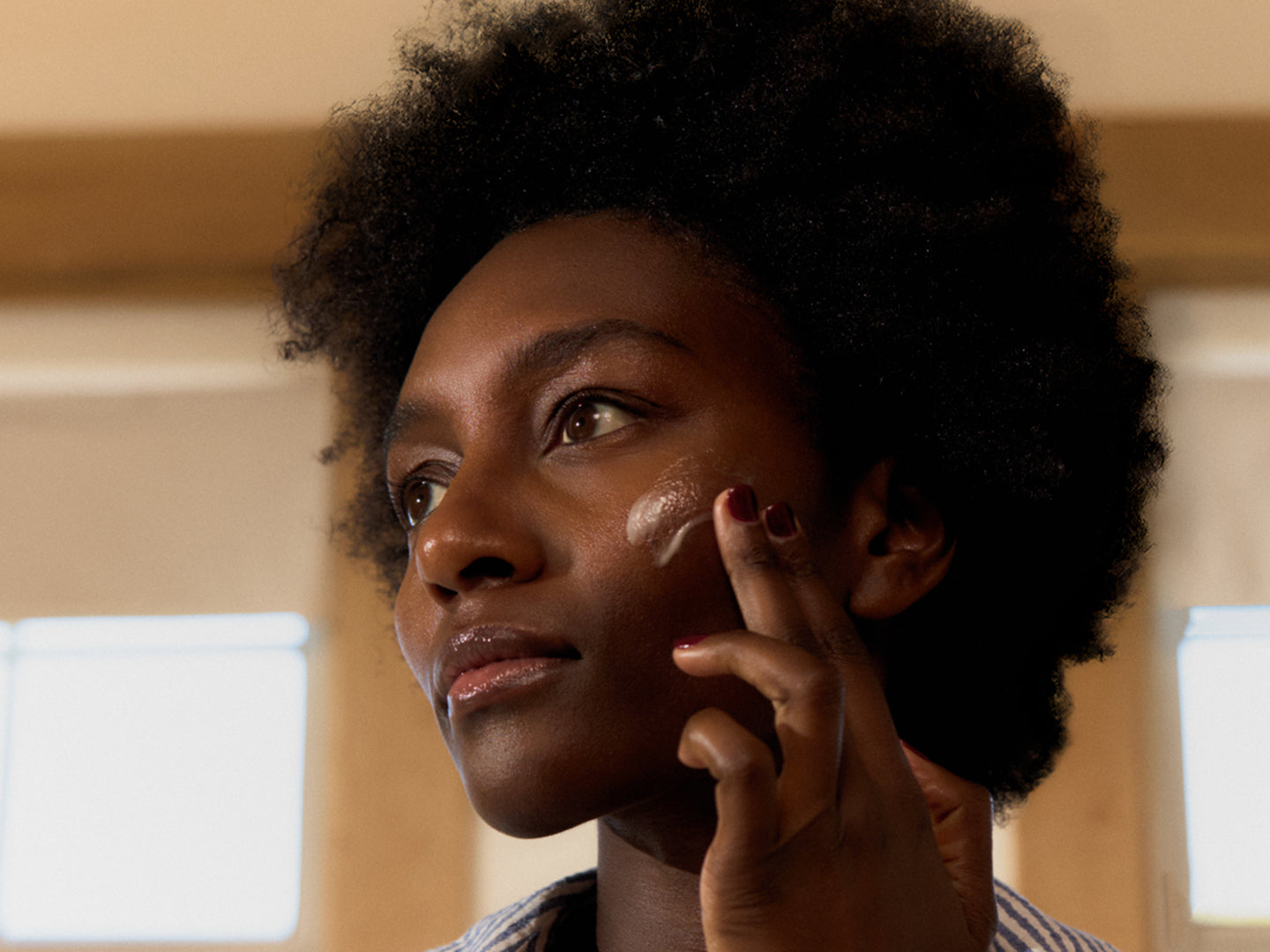 Woman applying moisturizer with a neutral background