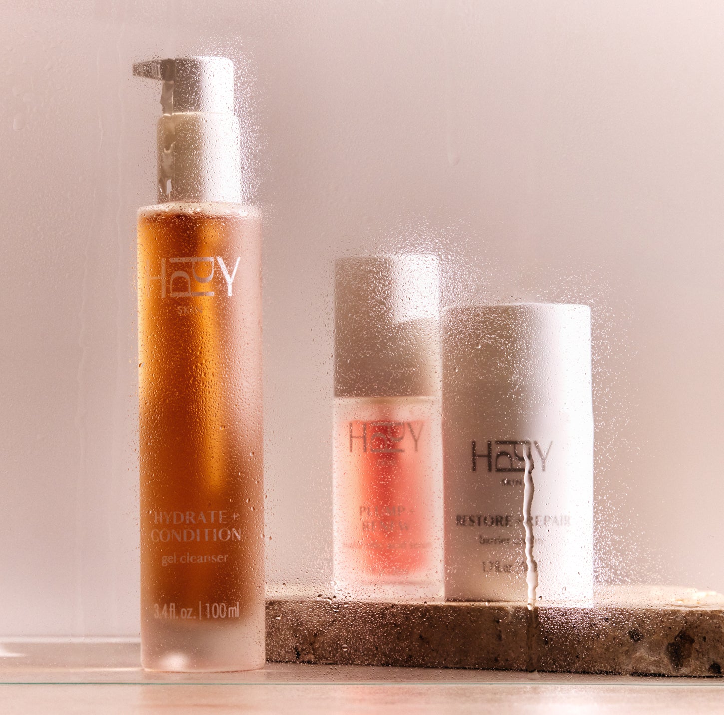 Three HPPY skincare products on a stone surface with a neutral background