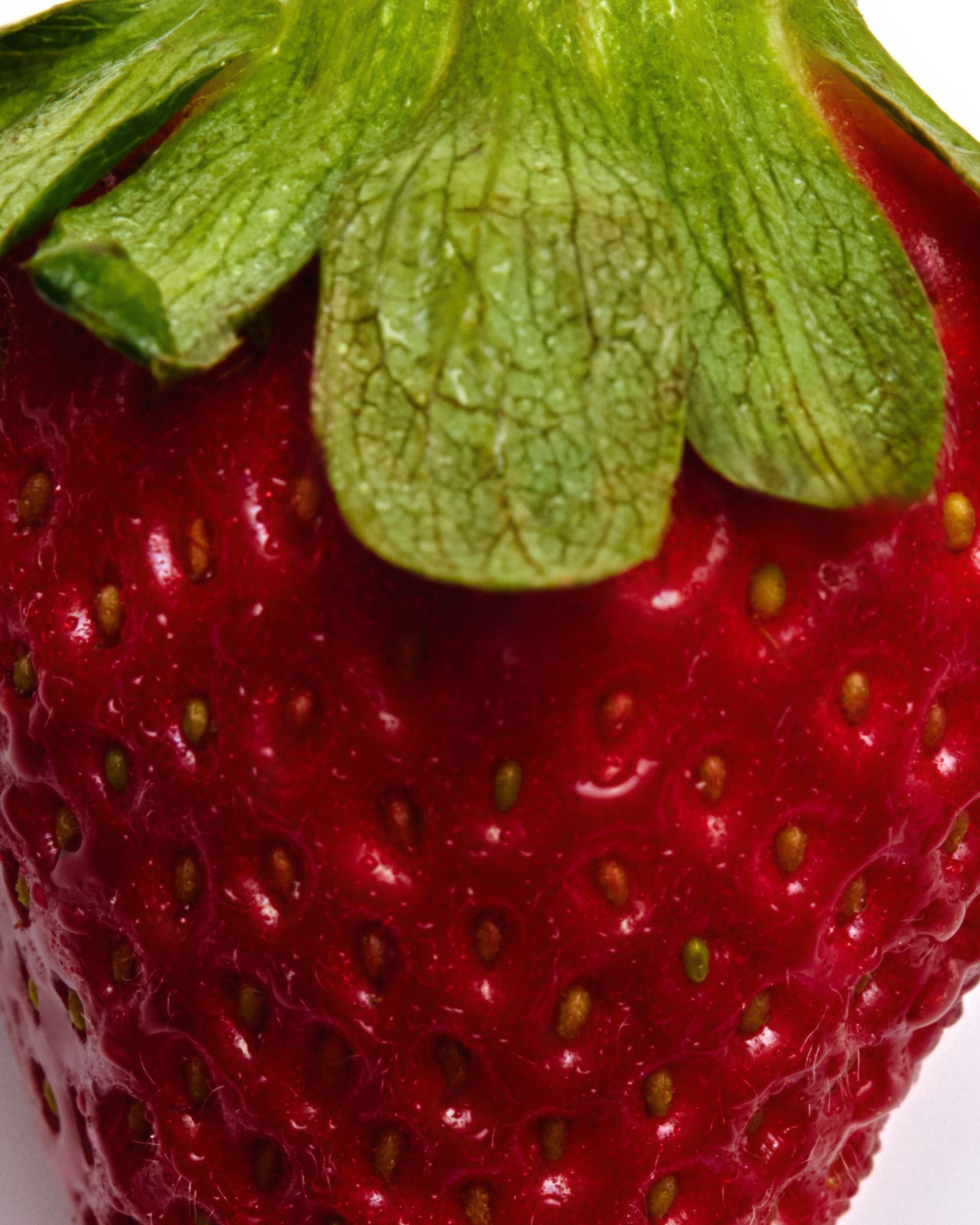 Close-up of a red strawberry with green leaves on a white background