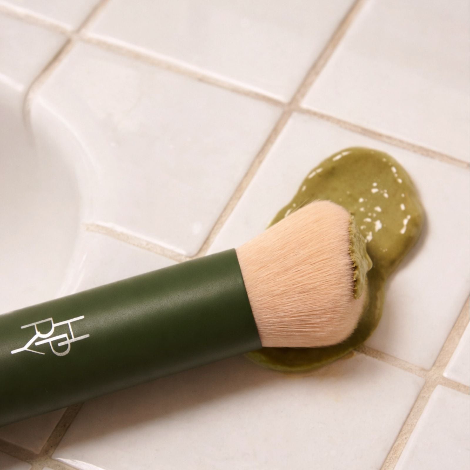 Makeup brush with green cosmetic product on a tiled floor