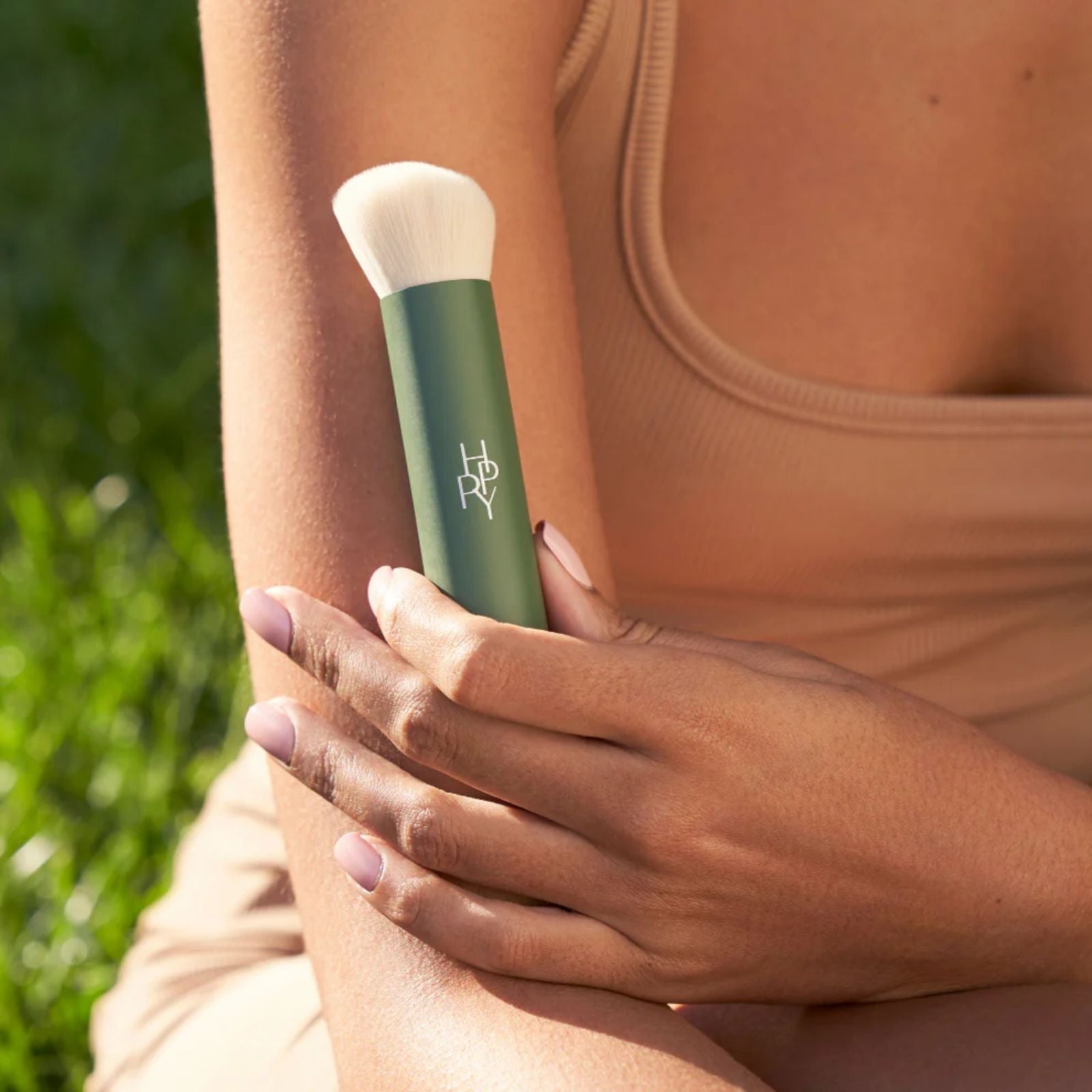 Person holding a green makeup brush with a blurred natural background