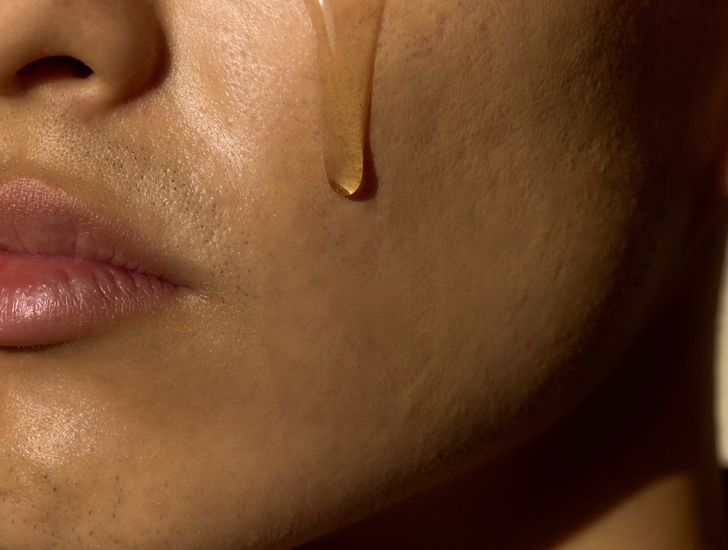Close-up of a person's face with a drop of honey dripping from their cheek.