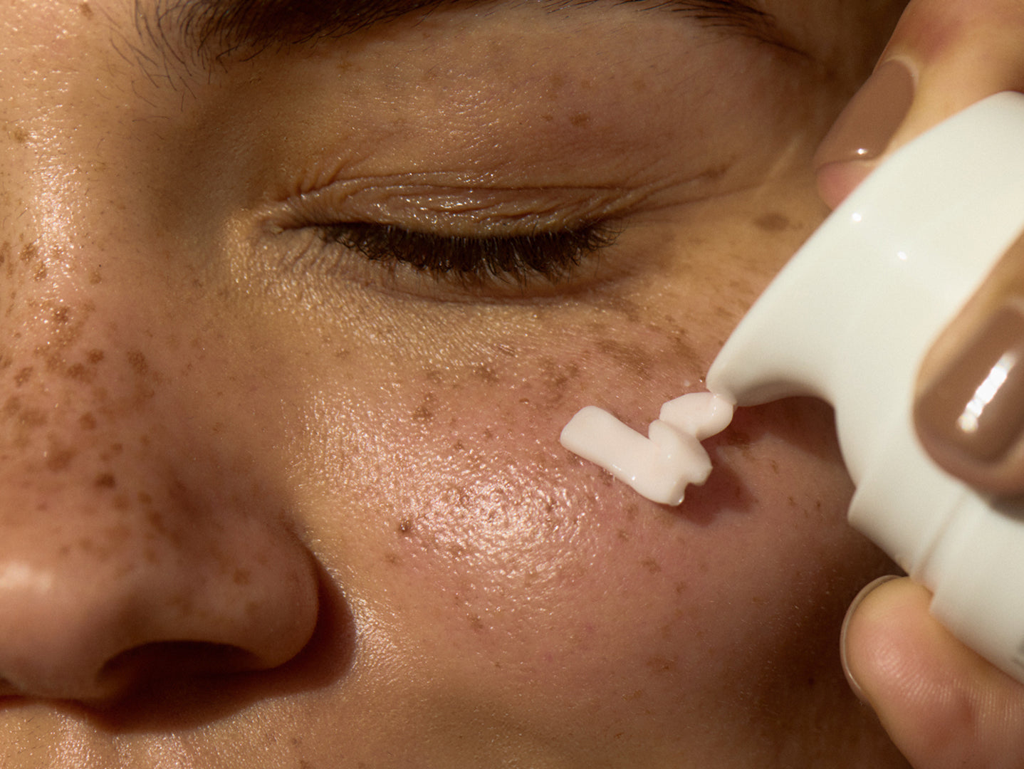 Person applying a white cream or gel to their face with a close-up focus on the skin texture.