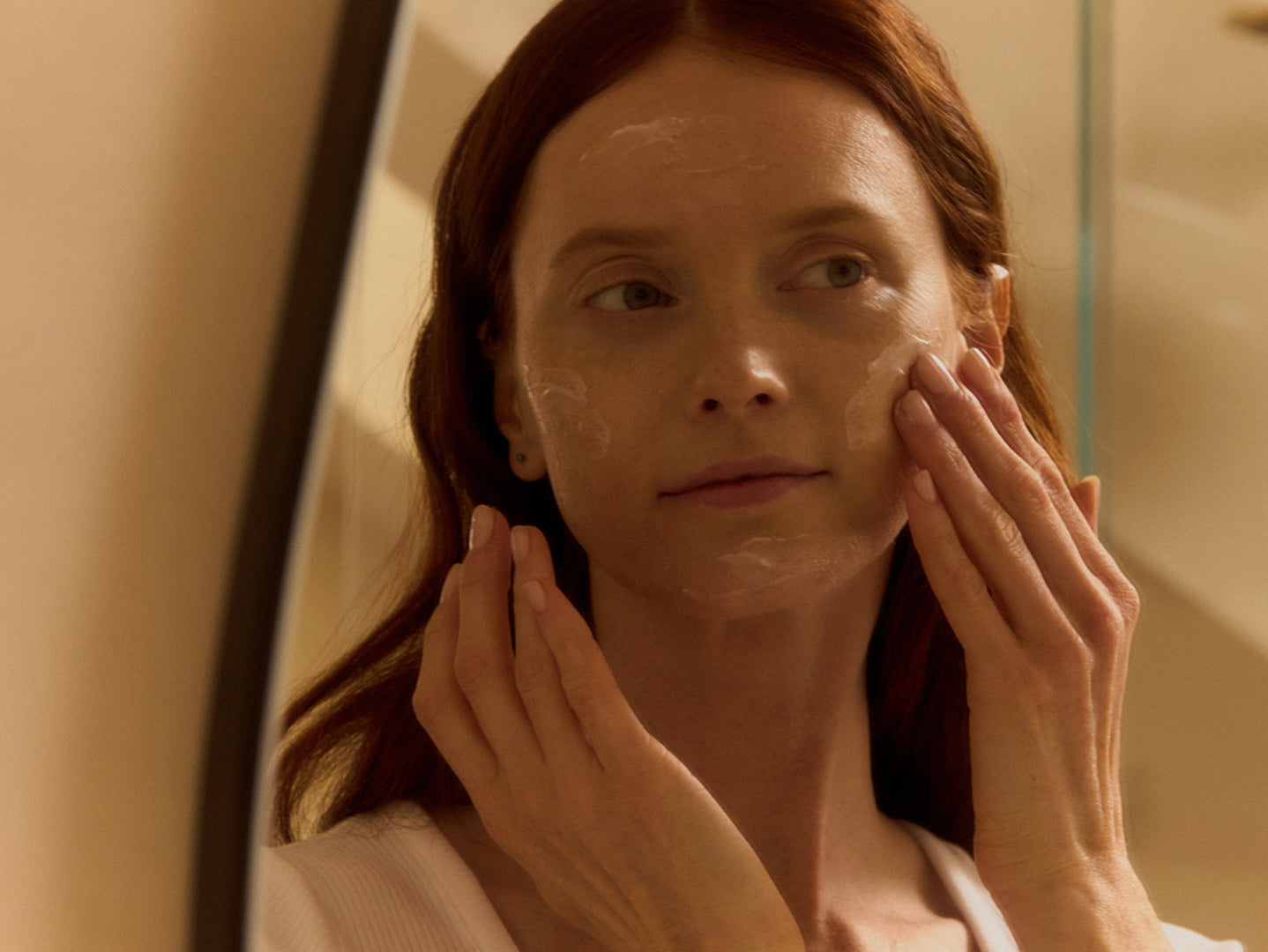 Woman applying cream to her face in front of a mirror