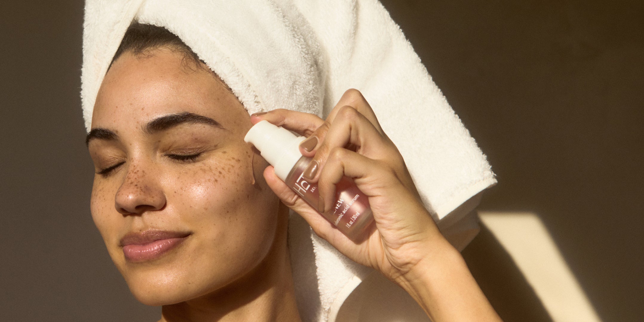 Woman applying skincare product with a towel on her head