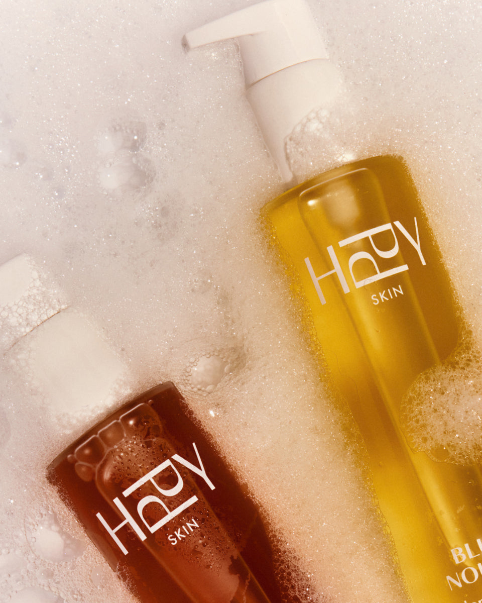Two bottles of 'HPPY Skin' products on a textured surface with bubbles.