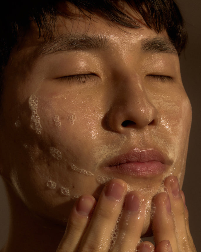 Person applying a facial cleanser with their fingers on a neutral background