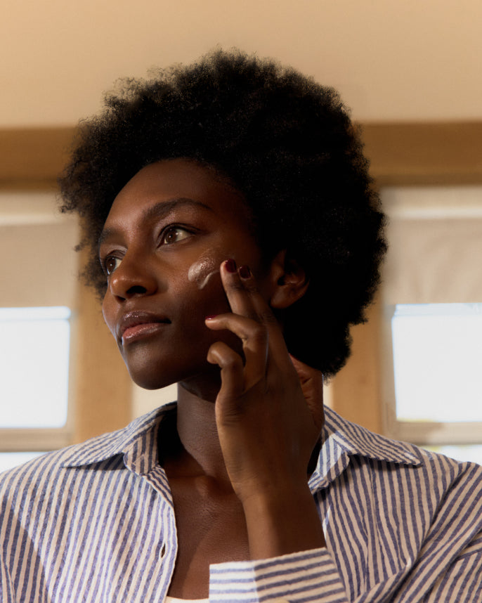 Woman applying cream to her face in a room with neutral colors