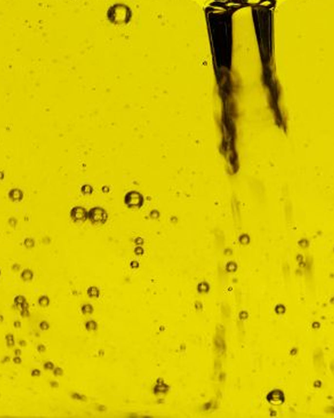 Close-up of olive oil with bubbles and a metallic object.