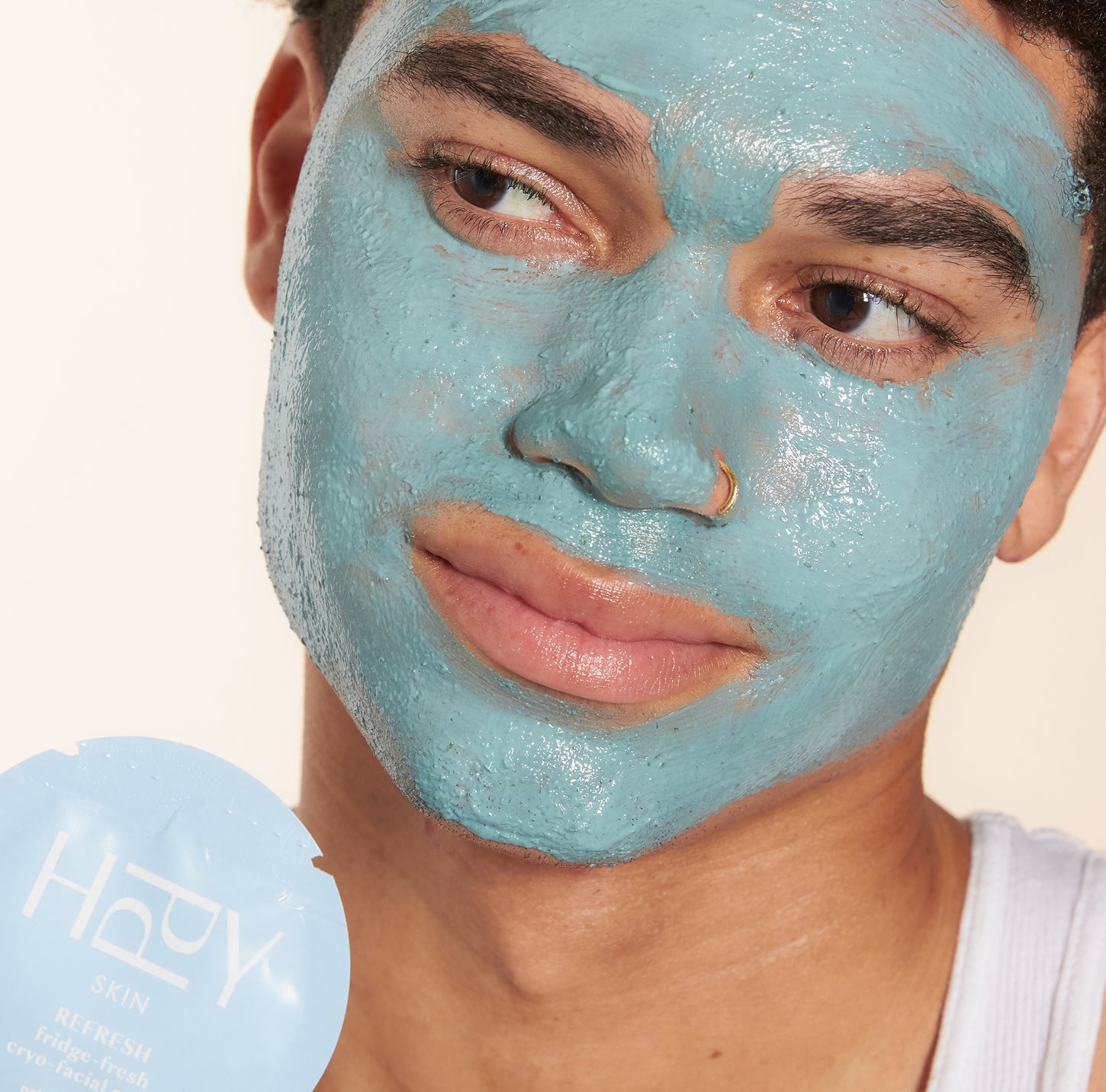 Person wearing a blue facial mask with a product container labeled 'HPPY' in the background.